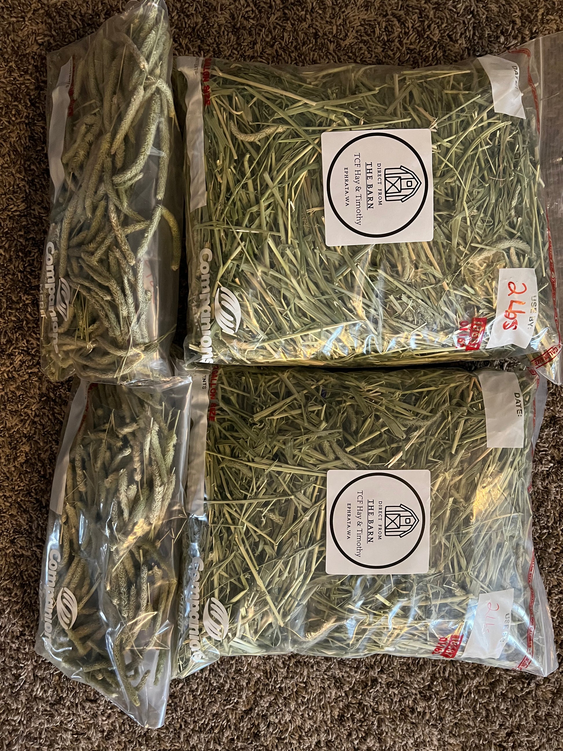 Four sealed plastic bags of Timothy hay and hay seed heads labeled from TCF The Barn, placed on carpet